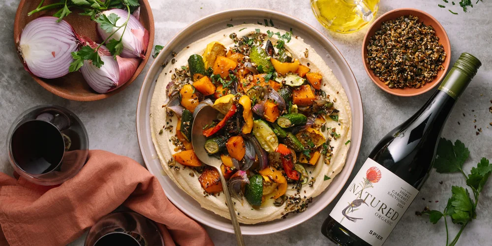 A bottle of Spier Good Natured Organic beside a plate of roast vegetables on hummus