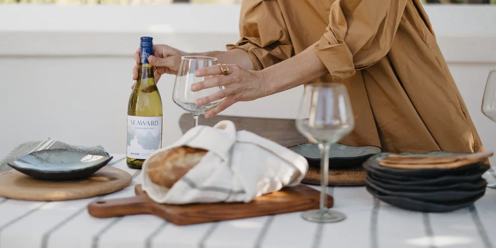 A bottle of Spier Seaward being set down on a table laid with bread and plates